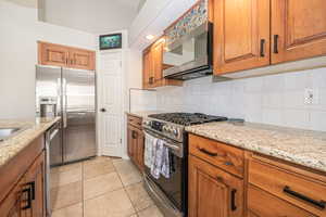 Kitchen with decorative backsplash, light tile patterned flooring, light stone countertops, and appliances with stainless steel finishes