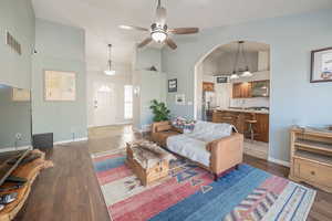 Living room with dark hardwood / wood-style flooring, vaulted ceiling, and ceiling fan