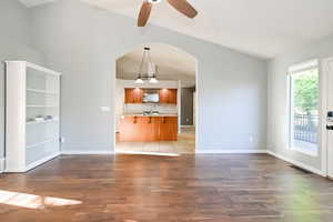 Unfurnished living room featuring lofted ceiling, arched walkways, light wood-style flooring, a sink, and a ceiling fan
