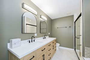 Full bath with a shower stall, double vanity, marble look tiles, toilet, and baseboards
