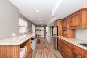 Kitchen featuring light wood-type flooring, light stone countertops, and stainless steel refrigerator