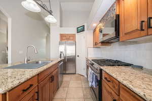 Kitchen featuring light stone countertops, stainless steel appliances, sink, decorative light fixtures, and light tile patterned flooring