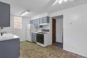 Kitchen featuring white fridge, sink, gray cabinets, ceiling fan, and gas range oven