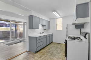 Kitchen with sink, wall chimney exhaust hood, range with gas stovetop, and gray cabinetry