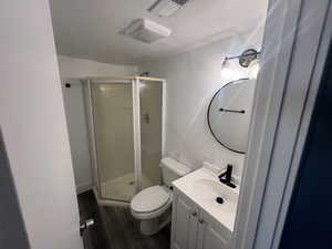 Bathroom featuring hardwood / wood-style floors, vanity, toilet, and a shower with door