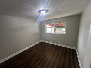 Empty room with a textured ceiling and dark hardwood / wood-style floors