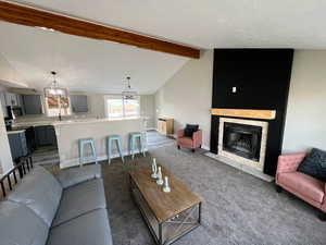 Living room featuring dark colored carpet, lofted ceiling with beams, and a notable chandelier