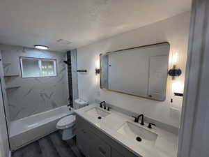 Full bathroom with hardwood / wood-style floors, a textured ceiling, toilet, vanity, and tiled shower / bath