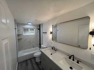 Full bathroom featuring vanity, tiled shower / bath combo, toilet, a textured ceiling, and wood-type flooring