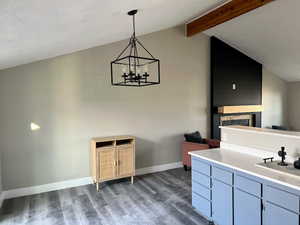 Interior space featuring vaulted ceiling with beams, dark wood-type flooring, hanging light fixtures, and an inviting chandelier