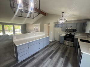 Kitchen with appliances with stainless steel finishes, sink, lofted ceiling with beams, decorative light fixtures, and an inviting chandelier