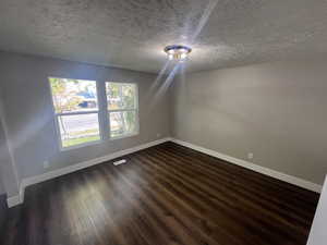 Unfurnished room featuring dark wood-type flooring and a textured ceiling