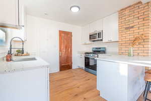 Kitchen with white cabinets, sink, light stone countertops, light hardwood / wood-style floors, and stainless steel appliances