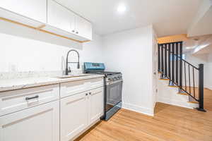 Kitchen with light stone countertops, sink, light hardwood / wood-style floors, white cabinetry, and stainless steel range with gas stovetop