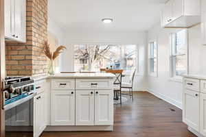 Kitchen with dark hardwood / wood-style flooring, light stone counters, white cabinetry, and high end stainless steel range oven