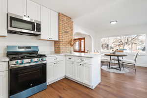 Kitchen with hardwood / wood-style floors, white cabinetry, light stone counters, kitchen peninsula, and stainless steel appliances