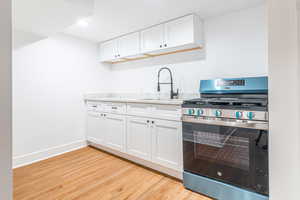 Kitchen featuring light stone countertops, sink, stainless steel gas range oven, light hardwood / wood-style flooring, and white cabinets