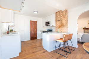 Kitchen featuring sink, appliances with stainless steel finishes, a kitchen bar, white cabinets, and light wood-type flooring