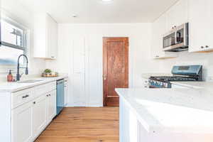 Kitchen featuring white cabinets, sink, light stone countertops, light hardwood / wood-style floors, and stainless steel appliances