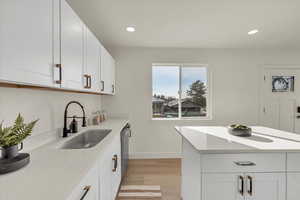 Kitchen with dishwasher, sink, white cabinets, and light hardwood / wood-style flooring