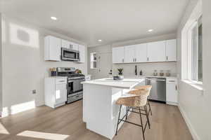 Kitchen featuring white cabinetry, appliances with stainless steel finishes, a breakfast bar area, a kitchen island, and light wood-type flooring