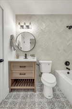 Full bathroom with tile patterned floors, vanity, tiled shower / bath combo, and toilet