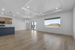 Unfurnished living room featuring an inviting chandelier, sink, a raised ceiling, and light wood-type flooring