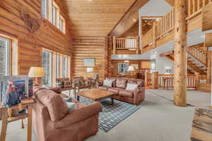 Living room featuring wooden ceiling, light carpet, high vaulted ceiling, ceiling fan, and rustic walls