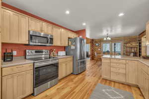 Kitchen featuring rustic walls, light brown cabinets, stainless steel appliances, light hardwood / wood-style flooring, and decorative light fixtures