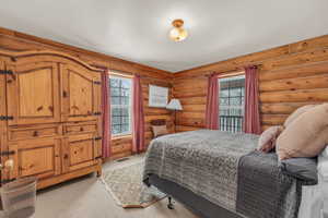 Carpeted bedroom with rustic walls and multiple windows