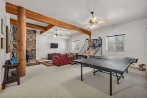 Recreation room with beamed ceiling, carpet flooring, a wood stove, and ceiling fan