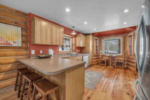 Kitchen featuring hanging light fixtures, light brown cabinetry, log walls, a breakfast bar area, and stainless steel appliances