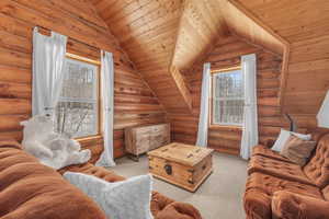 Living room with log walls, light colored carpet, vaulted ceiling, and wooden ceiling