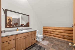 Bathroom featuring vanity, log walls, vaulted ceiling, and toilet