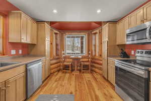 Kitchen with sink, light brown cabinets, log walls, stainless steel appliances, and light hardwood / wood-style floors