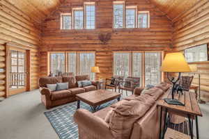 Carpeted living room featuring log walls, high vaulted ceiling, and wood ceiling