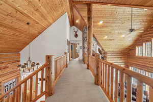 Hallway with rustic walls, a chandelier, wood ceiling, and vaulted ceiling