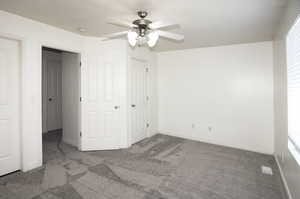 Unfurnished bedroom with dark carpet and ceiling fan