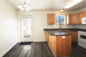 Kitchen featuring dark hardwood / wood-style flooring, a notable chandelier, kitchen peninsula, pendant lighting, and white appliances