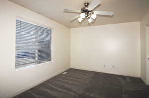 Empty room with ceiling fan and dark carpet