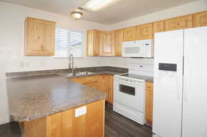 Kitchen with sink, dark wood-type flooring, kitchen peninsula, white appliances, and light brown cabinetry