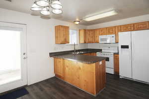 Kitchen with white appliances, sink, hanging light fixtures, dark hardwood / wood-style floors, and kitchen peninsula