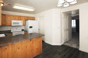 Kitchen with kitchen peninsula, dark hardwood / wood-style flooring, white appliances, and a textured ceiling