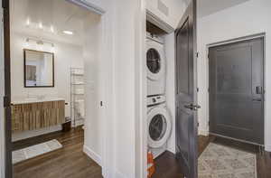 Laundry area featuring dark hardwood / wood-style floors, stacked washer / drying machine, and sink