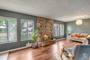 Living room with hardwood / wood-style floors, a textured ceiling, and a stone fireplace