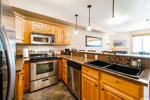 Kitchen featuring sink, stainless steel appliances, kitchen peninsula, dark stone countertops, and pendant lighting