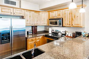 Kitchen with sink, light stone countertops, stainless steel appliances, and hanging light fixtures