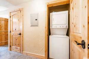 Washroom with stacked washing maching and dryer, carpet floors, and electric panel