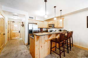 Kitchen featuring light carpet, a kitchen breakfast bar, light brown cabinetry, kitchen peninsula, and stainless steel appliances