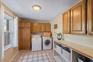 Laundry area featuring washer and dryer, light tile patterned floors, and cabinets